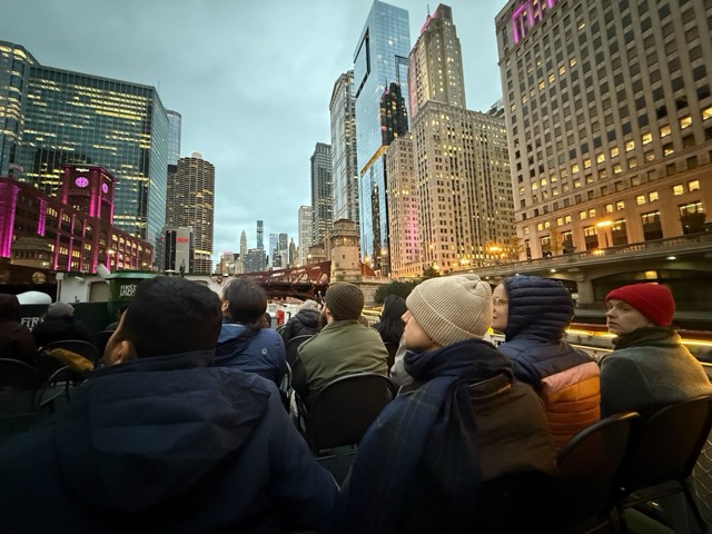 The Amuse team on an architecture boat tour along the Chicago River at dusk, surrounded by city skyscrapers.
