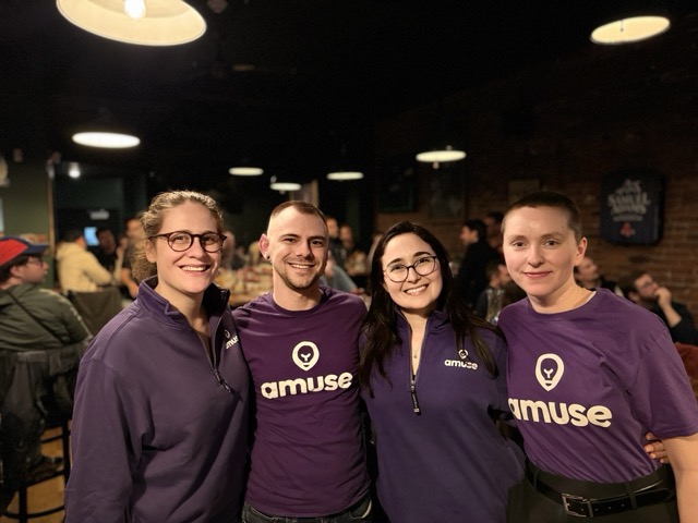 Four Amuse team members smiling together in matching purple Amuse t-shirts.